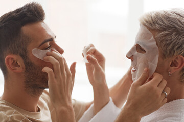 Side view close up of young gay couple applying face masks on each other while enjoying morning beauty routine