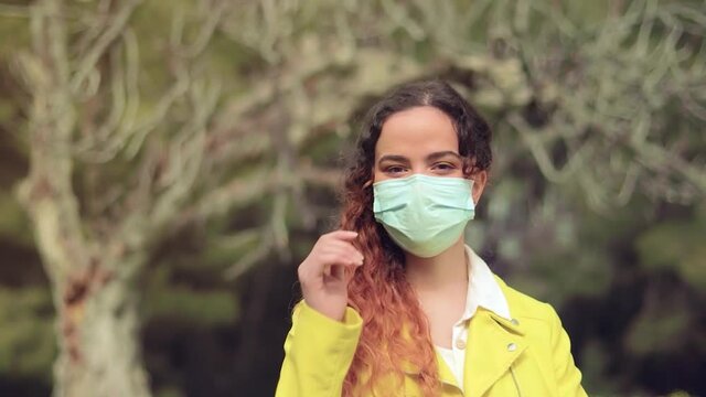 mujer se quita la mascarilla delante de las ramas de un &aacute;rbol en un bosque
