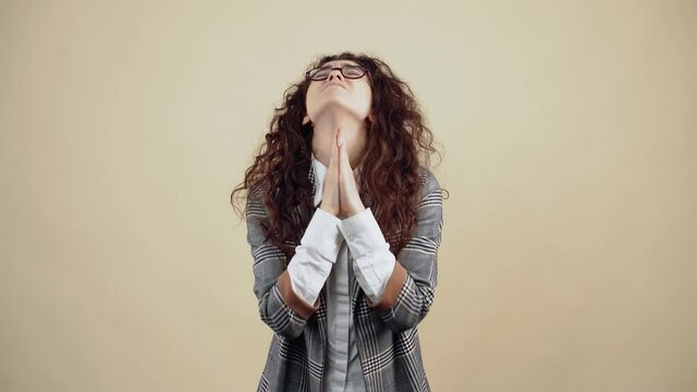 The desperate young woman, with her hands clasped, asks for help and insists strongly on helping her. Cretaceous in gray jacket and white shirt, with glasses posing isolated on a beige background in