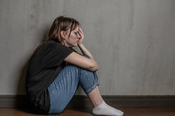 Crying teen girl sits on the floor near a wall