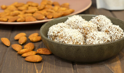 Marzipan candy being covered with grated coconut on wooden background. Round white candy with coconut flakes. Homemade snacks. Healthy food for weekdays and holidays