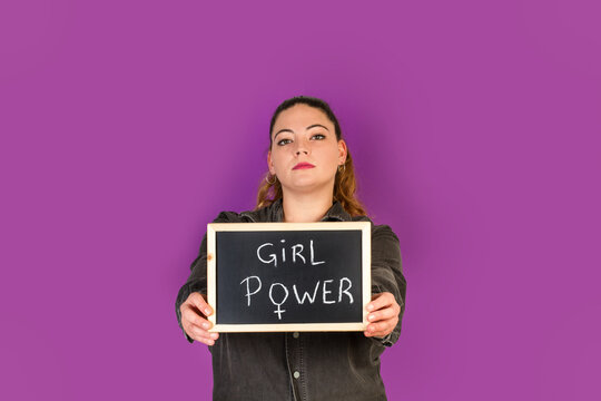 Mujer joven sosteniendo una pizarra con la palabra escrita Girl Power sobre un fondo morado liso y aislado. Vista de frente. Copy space