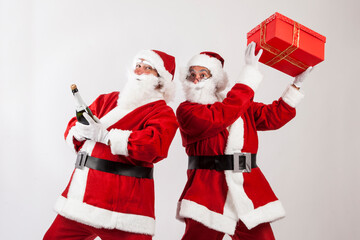 coppia di babbi natale gioca e scherza con in mano  un regalo color rosso e una bottiglia di spumante , isolati su sfondo bianco