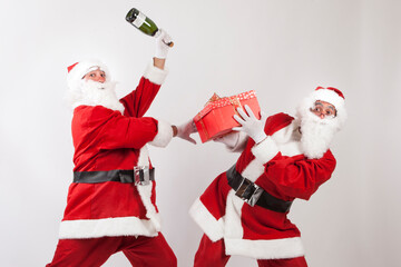 coppia di babbi natale gioca e scherza con in mano  un regalo color rosso e una bottiglia di...