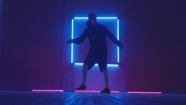 Person in windbreaker and red cap dancing to breakdance. blue rectangle neon background . Flickering neon background . man dancing to breakdance in night club