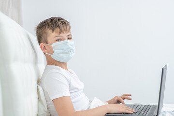 Sick boy wearing protective mask is engaged in distance learning with a laptop. Quarantine and coronavirus epidemic concept