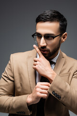 young arabian man in beige blazer pointing with finger while looking away isolated on grey