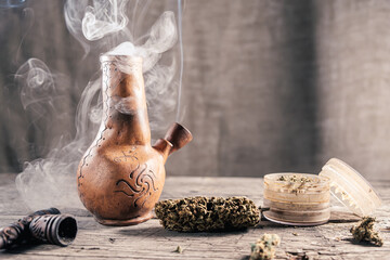 On the wooden surface is an old clay bong with medical marijuana that is smoking
