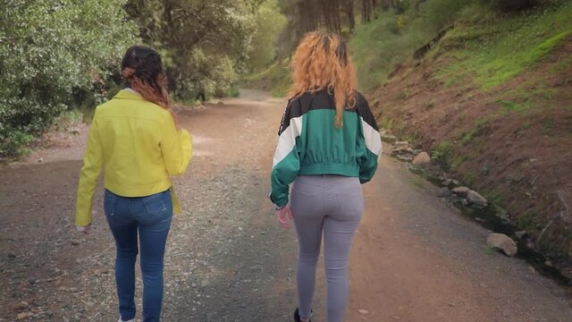 Dos hermanas gemelas pasean y charlan por un camino forestal en un bosque con &aacute;rboles en Espa&ntilde;a