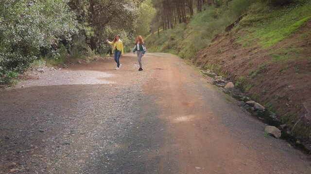 Dos hermanas gemelas pasean y charlan por un camino forestal en un bosque con &aacute;rboles en Espa&ntilde;a