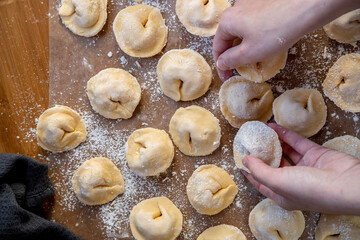 Pelmeni dumplings making process: Woman's hand taking raw, unccoked, pelmeni stuffed with meat filling. Gluten free recipe for traditional Russian cuisine. Floured wooden surface, handmade dumplings.