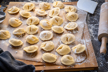 Pelmeni dumplings making process: Raw, uncooked, pelmeni stuffed with meat filling on a wooden, floured board. Gluten free recipe for traditional Russian cuisine. handmade ravioli or dumplings.