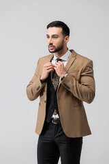 stylish arabian man adjusting tie while looking away isolated on grey