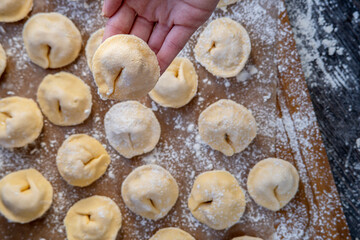 Pelmeni dumplings making process: Woman's hand showing raw pelmeni dough stuffed with meat filling. Gluten free recipe for traditional Russian cuisine. Floured wooden surface, handmade dumplings.