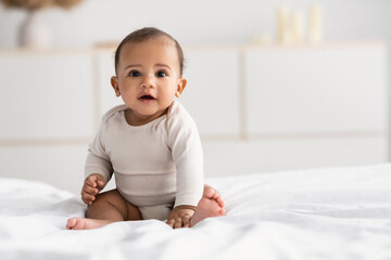 Cute little African American infant sitting on bed - Powered by Adobe