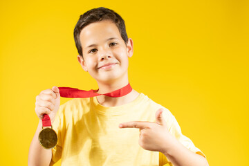 Young boy showing his golden medal over yellow background.