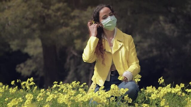 Mujer joven se quita la mascarilla y sonr&iacute;e al sol en un prado con flores amarillas