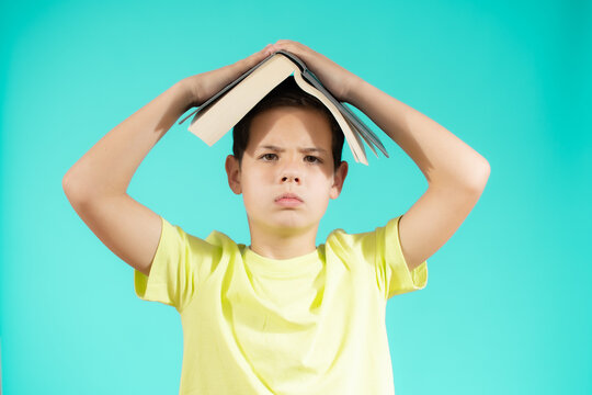 Portrait Of Serious Kid Holding Book Above Head, Stand Isolated Over Green Background Studio. Funny Education Concept