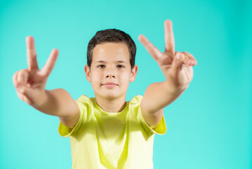 Portrait of little boy showing victory hands sign on green background
