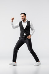 Fototapeta na wymiar Full length view of cheerful Muslim man in trendy clothes and sneakers dancing on grey