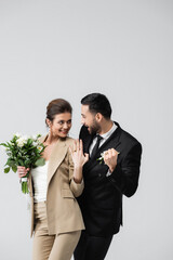 excited muslim groom showing win gesture while looking at cheerful bride isolated on grey