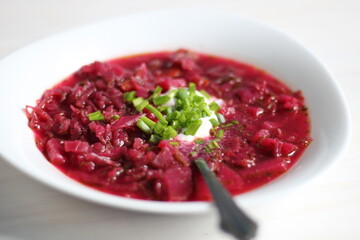 red beet soup borsch with scallion, sour cream, spoon in plate on white table