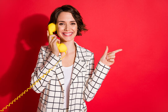 Photo of young cheerful girl talk cable phone happy smile point finger empty space ad recommend isolated over red color background