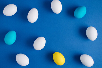 Yellow, white and light blue eggs on a blue background. Minimal Easter or food layout. Creative holiday concept. Flat lay