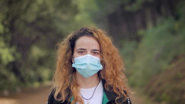 mujer joven gemela se quita la mascarilla y sonr&iacute;e de alegr&iacute;a en un bosque con &aacute;rboles en el fondo