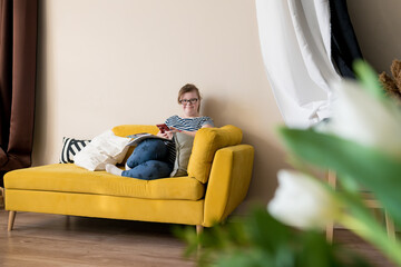 Portrait of smiling teenager girl with Down syndrome using smartphone while sitting on sofa in living room at home. Domestic life of people with disabilities. - Powered by Adobe