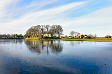 Obraz premium The 12th century romanesque Saint Nicholas Church on mound in Hijum Friesland with outdoor ice-skating rink in front during winter.