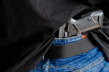 Hided handgun under the denim belt. A person is hiding a handgun under the denim belt.