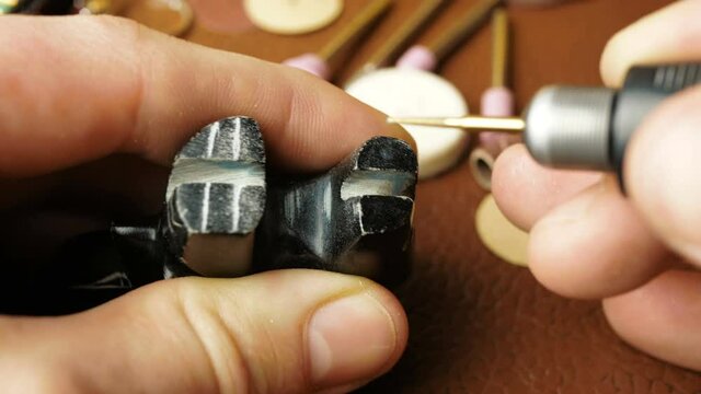 A professional jeweler engraves on a stone figurine to create a piece of jewelry.