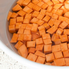 Diced sweet potatoes soaking on a counter in a gray bowl of water waiting to be cooked in a home kitchen.