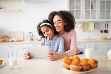 Obraz na płótnie Canvas Black woman and girl using tablet in kitchen