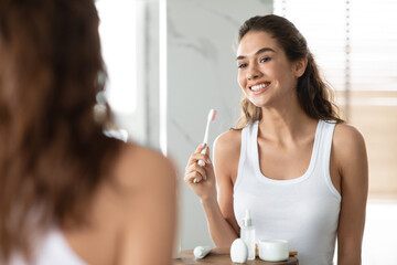 Obraz na płótnie Canvas Woman Brushing Teeth Holding Toothbrush Smiling To Mirror In Bathroom