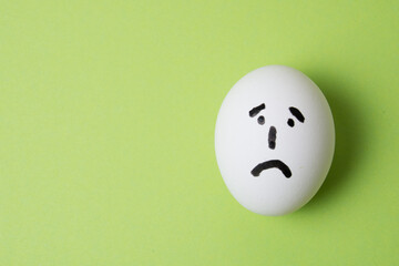 Egg with a sad face, on a green background with copy space