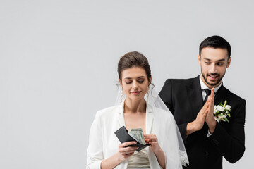 Tricky arabian groom standing near bride with dollars isolated on grey