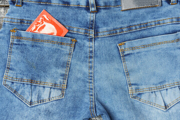 condom in the pocket of blue jeans. condom in a red package.