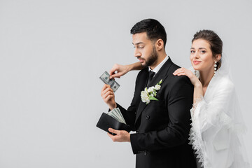 Smiling bride taking currency from muslim groom isolated on grey