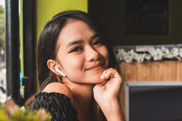 A friendly young Filipina lady with a faint smile while listening to music on wireless headphone...