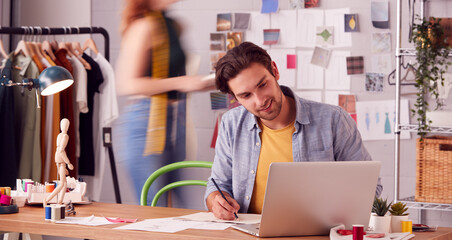 Male And Female Business Owners Working On Designs In Busy Fashion Studio Together