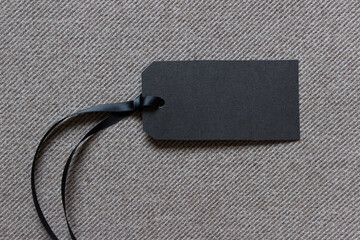 Horizontal blank black paper price label on textured striped fabric with satin rope. Photo with...