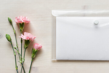 Mockup template with pink flowers and blank paper in plastic folder on wooden background. 