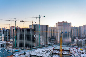 Construction site, cranes and multi-storey unfinished buildings at sunrise or sunset in winter