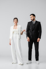 Muslim groom in handcuffs looking at cheerful bride on white background