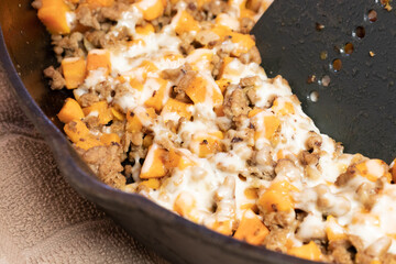 Ground turkey meat, cubed sweet potatoes, melted mozzarella cheese, and diced onions served for dinner in a cheesy, nutritious cast iron skillet meal in a home kitchen.