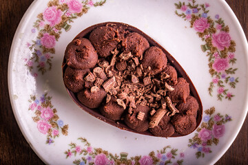 Top view of mini stuffed chocolate easter egg with grated chocolate on the top on a white plate with flowers design on a wooden table.