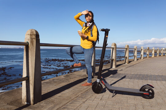 African american woman shading from sun eating sandwich on promenade by the sea
