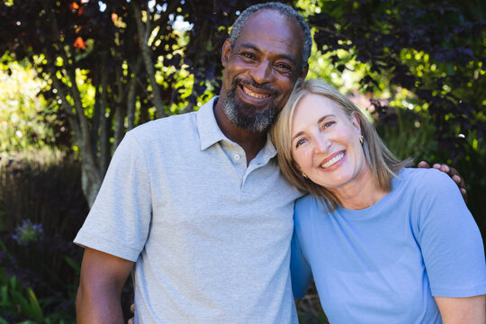 Portrait Of Diverse Senior Couple In Garden Looking At Camera And Smiling